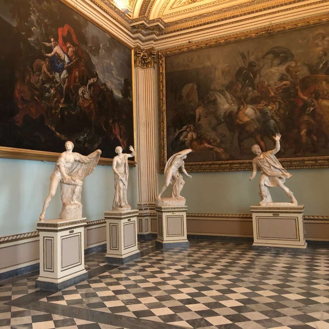 Four sculptures and two large painting in a corner of a room at the UIffizi in Florence